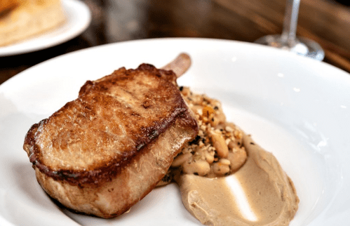 A beautifully cooked pork chop served with white beans and a creamy sauce on a white plate.