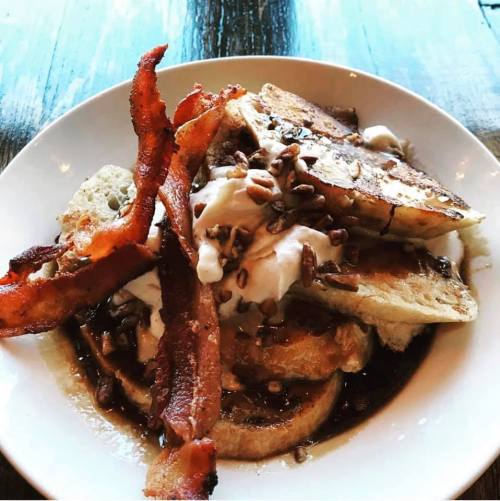 A bowl of French toast topped with yogurt, nuts, and crispy bacon strips.