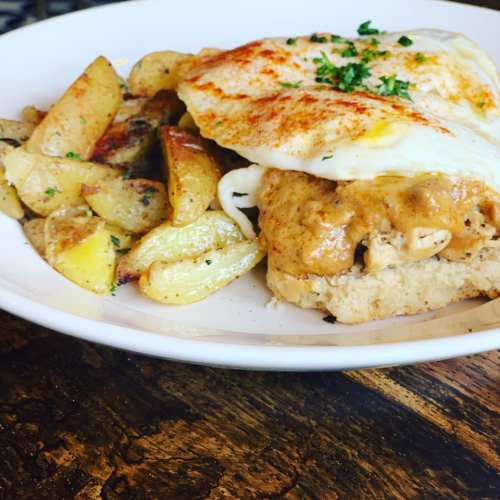 A plate of chicken and gravy over bread, topped with eggs, served with seasoned roasted potatoes on the side.