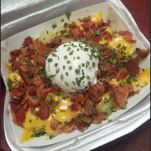 A container of loaded nachos topped with cheese, bacon bits, and a dollop of sour cream, garnished with chives.