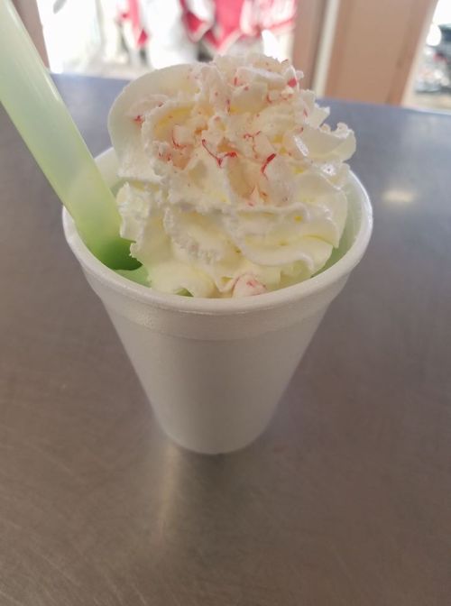 A frosty green drink topped with whipped cream and crushed peppermint in a white cup with a green straw.
