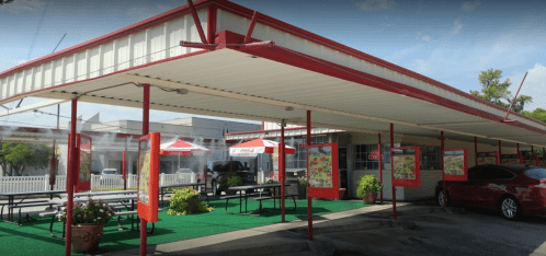 A colorful outdoor dining area with red umbrellas, picnic tables, and a covered walkway at a restaurant.