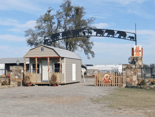A small, decorated building with a cattle-themed archway, surrounded by gravel and trees under a blue sky.