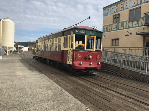 A vintage streetcar in red and yellow parked on a wooden platform near a historic building.