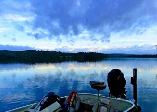 A serene lake at dusk, reflecting clouds and trees, with a boat in the foreground.