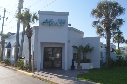 Exterior of a modern building with the sign "Alfie's," surrounded by palm trees and a clear blue sky.
