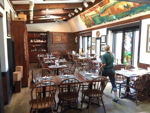 A cozy restaurant interior with wooden tables, chairs, and colorful artwork on the walls. A server is walking through.