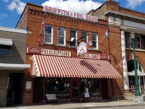 Historic brick drugstore with a striped awning, displaying "Griffith & Feil Drug" and "Open" signs.