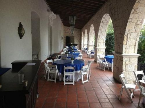 A spacious outdoor area with arched stone walls, featuring tables set with blue tablecloths and white chairs.