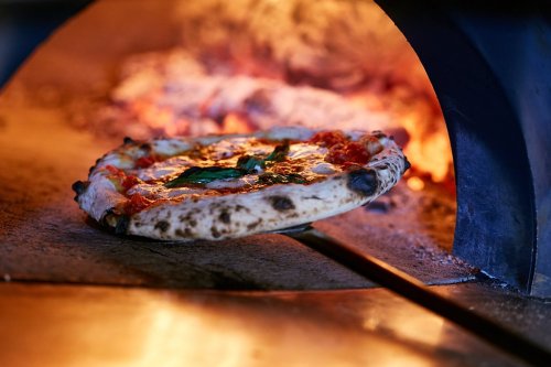 A freshly baked pizza with basil being pulled from a wood-fired oven.