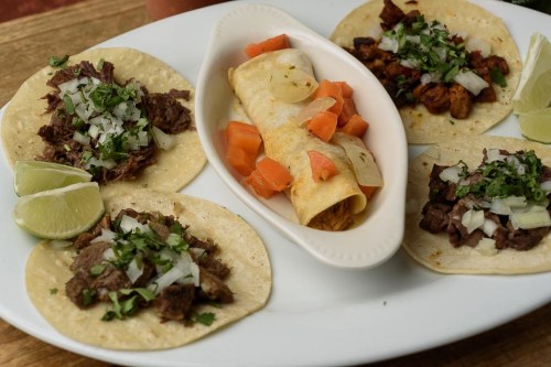 A plate of tacos with beef, onions, and cilantro, alongside a rolled taco filled with meat and diced vegetables.