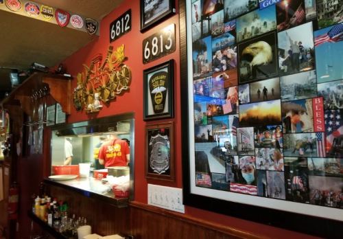 A cozy restaurant interior featuring a wall of photos, badges, and memorabilia, with a service counter in the foreground.