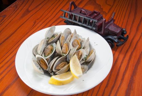 A plate of steamed clams garnished with lemon, next to a decorative red fire truck on a wooden table.