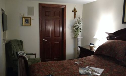 Cozy bedroom with a patterned bedspread, wooden furniture, a door, and decorative elements like a cross and flowers.
