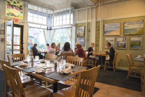 A cozy restaurant interior with wooden tables, diners enjoying meals, and artwork on the walls. Natural light filters in.