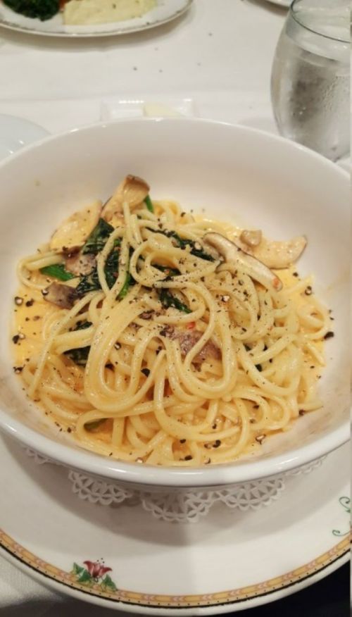 A bowl of pasta with mushrooms and greens, topped with grated cheese and black pepper, served on a decorative plate.