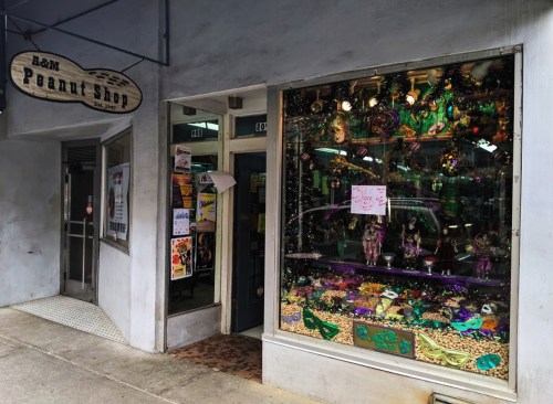 Exterior of A&M Peanut Shop with a colorful window display featuring Mardi Gras decorations and various snacks.