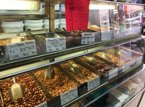 A display case filled with various seeds and nuts, labeled with prices for sunflower seeds, pumpkin seeds, and almonds.