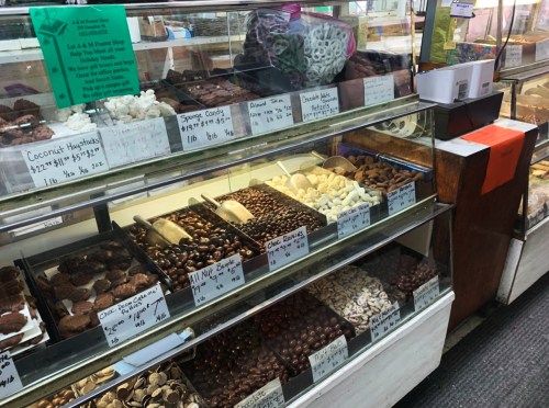 A display case filled with various chocolates and candies, labeled with prices and descriptions.