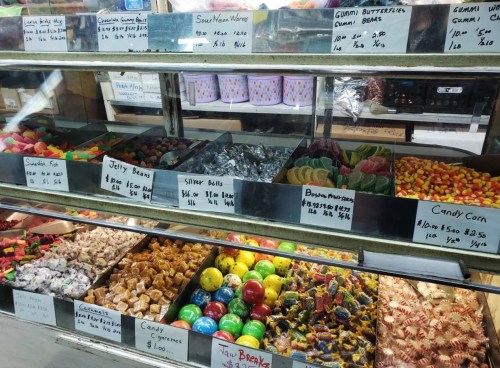A colorful display of various candies in a shop, including gummies, jelly beans, and sour treats, with price labels.