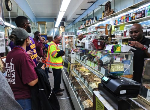 A busy shop with customers at the counter, browsing various snacks and treats, while staff assist them.