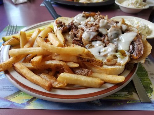 A plate of loaded fries with a cheesy beef sandwich and a side of coleslaw on a colorful table setting.