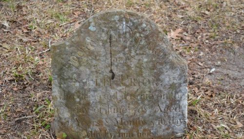 Weathered gravestone with inscriptions, partially obscured, marking the resting place of Peter Price, who died in 1765.