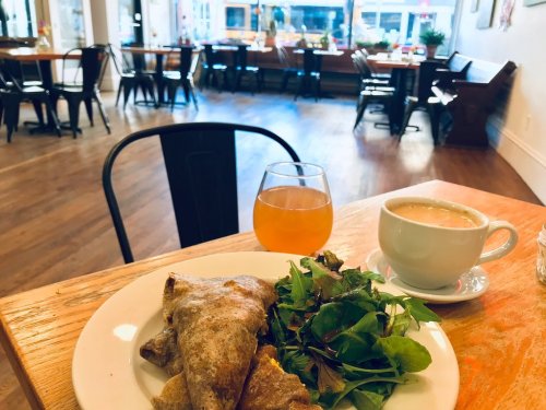 A plate with a savory crepe, salad, a cup of coffee, and a glass of orange drink in a cozy café setting.