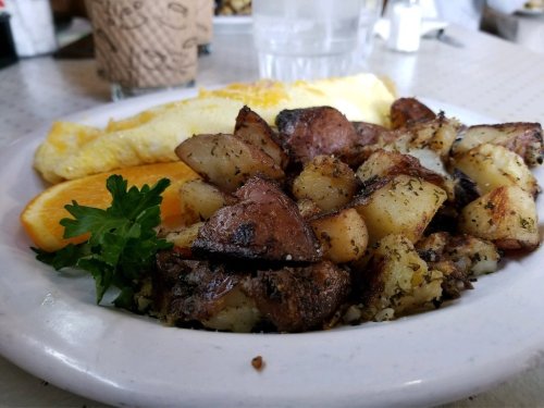 A plate of golden omelette, seasoned roasted potatoes, and a slice of orange, garnished with parsley.