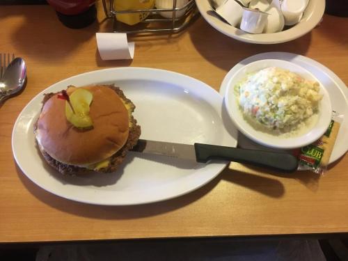 A plate with a fried chicken sandwich topped with pickles and a side of coleslaw. A knife rests beside the sandwich.