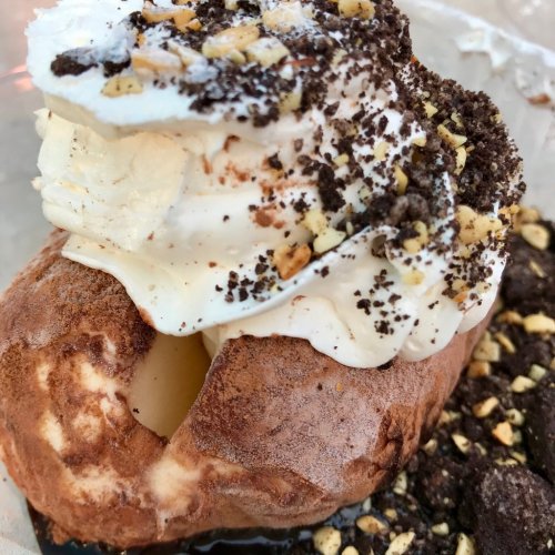 A close-up of a dessert featuring a chocolate-covered pastry filled with cream, topped with whipped cream and crushed nuts.