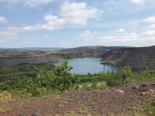 A scenic view of a lake surrounded by rocky cliffs and greenery under a partly cloudy sky.