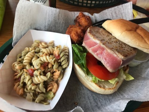 A plate featuring a tuna sandwich with lettuce and tomato, pasta salad, and two fried bites on the side.