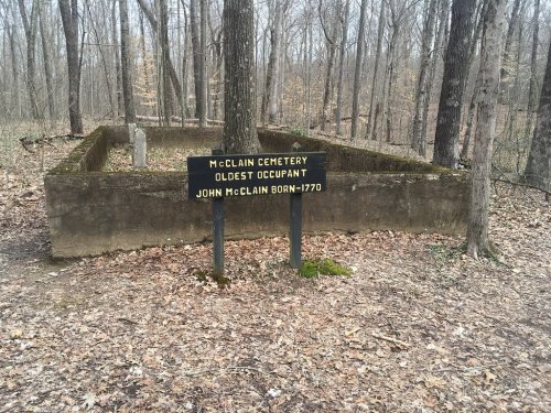 Sign marking McClain Cemetery, noting the oldest occupant, John McClain, born in 1770, surrounded by trees.