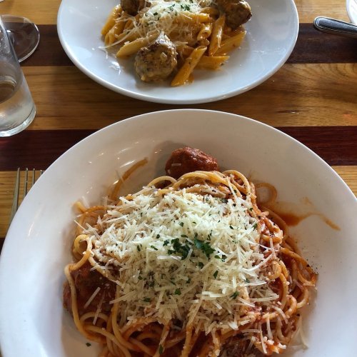 A plate of spaghetti topped with marinara sauce and grated cheese, with a second plate of penne and meatballs in the background.