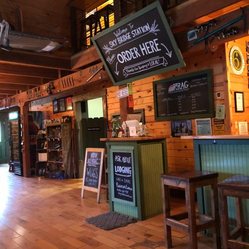 Interior of a rustic lodge with wooden walls, a welcome sign, and a menu board. Cozy and inviting atmosphere.