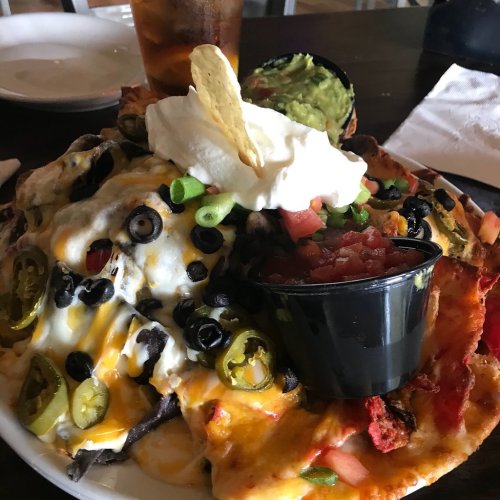A large plate of nachos topped with cheese, olives, jalapeños, guacamole, sour cream, and diced tomatoes.
