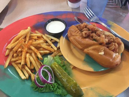 A colorful plate with a fried chicken sandwich, fries, a pickle, lettuce, and onion, alongside a small cup of dipping sauce.