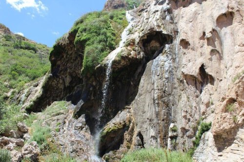 A scenic waterfall cascading down a rocky cliff, surrounded by lush greenery and blue skies.