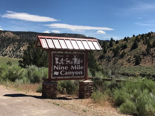 Welcome sign for Nine Mile Canyon, surrounded by green hills and blue skies.