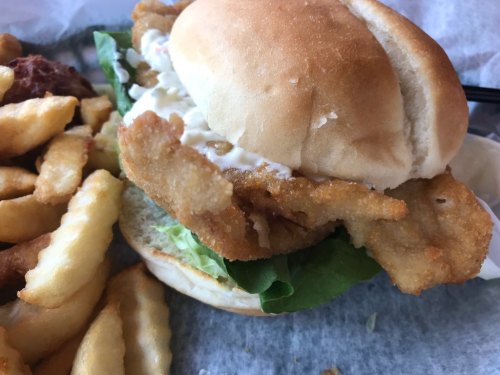 A crispy fish sandwich with lettuce and mayonnaise, served with crinkle-cut fries on the side.
