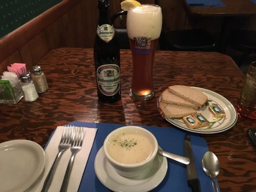 A table setting with a beer, a bowl of soup, slices of bread, and a plate of snacks in a cozy restaurant.