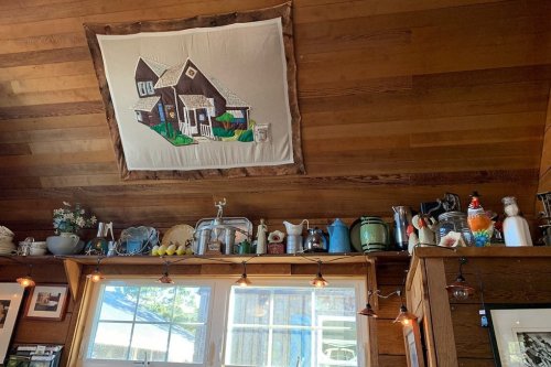 A cozy wooden interior with a quilted house hanging on the wall and various vintage kitchen items on shelves.