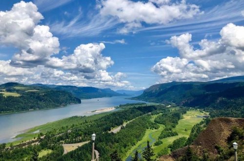 A scenic view of a river winding through lush green hills under a blue sky with fluffy white clouds.