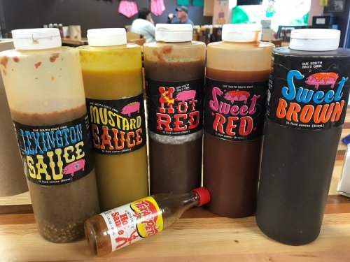 Five bottles of barbecue sauces labeled "Lexington Sauce," "Mustard Sauce," "Sweet Red," "Hot Red," and "Sweet Brown" on a table.