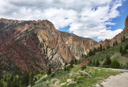 Scenic view of rugged mountains with colorful rock formations under a partly cloudy sky, alongside a winding road.