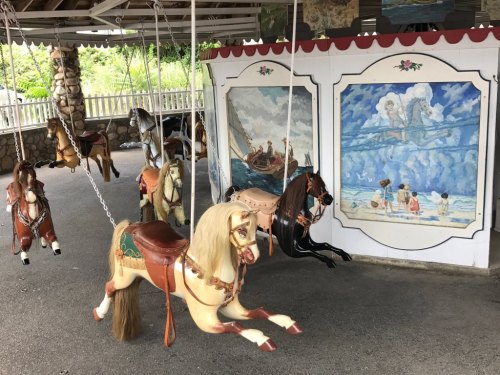 A vintage carousel with painted wooden horses and a mural depicting a beach scene in the background.