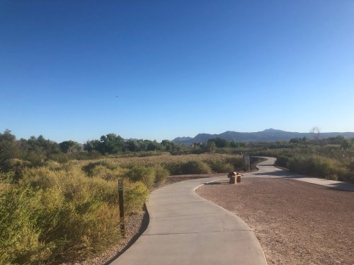 A winding path through a green landscape with mountains in the background under a clear blue sky.
