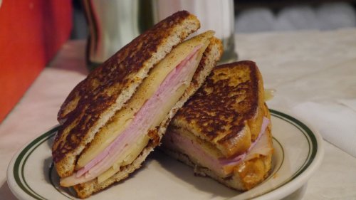 A grilled sandwich with layers of ham and cheese, served on a plate with a rustic table setting.