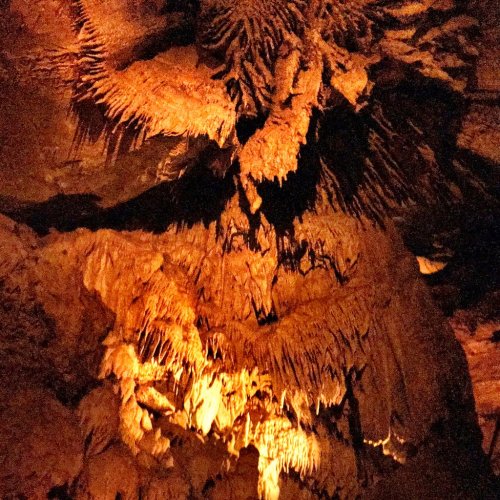 Stalactites and stalagmites illuminated in warm orange light inside a cave, showcasing intricate rock formations.